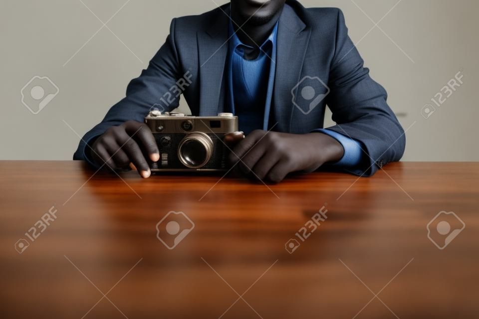 Przycięty obraz afrykańskiego mężczyzny w garniturze siedzącego przy stole z aparatem retro