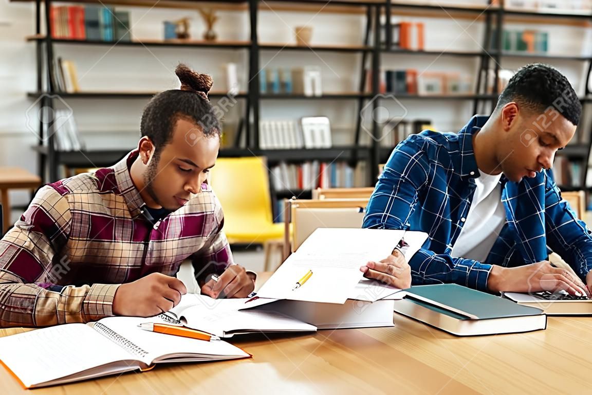 Twee gemengde race mannelijke studenten studeren met laptop terwijl zittend aan de bibliotheekbalie