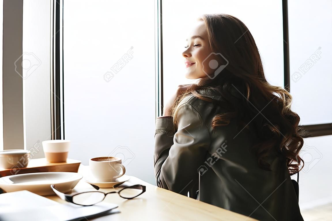 Photo de vue arrière de la jeune femme heureuse avec les cheveux longs, assis dans un café. Regardant de côté.