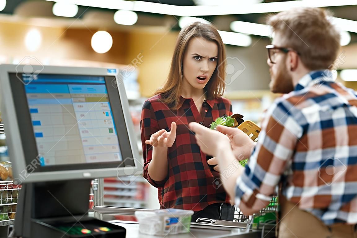 Photo of confused young lady standing in supermarket shop near cashier's desk. Looking aside.