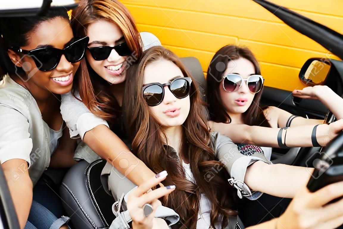 Bild von lächelnden emotionalen vier jungen Frauen , die Freunde im Auto sitzen . Selfie mit Handy