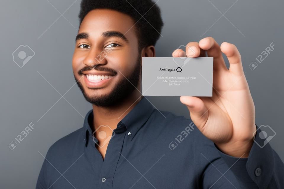 Sorrindo jovem afro americano cara mostrando cartão de visita em branco isolado sobre fundo cinza