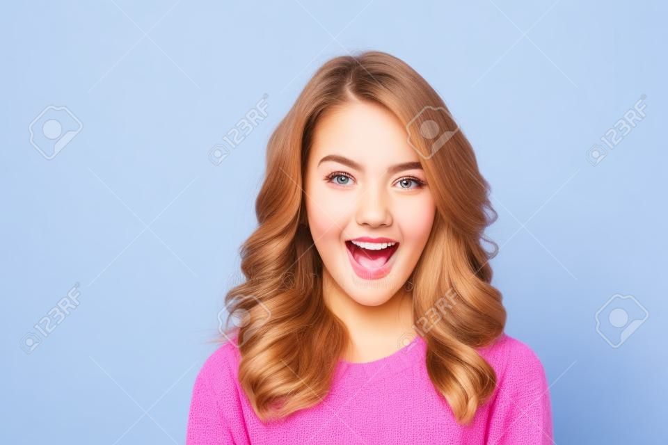 Close up portrait of a cheerful young girl dressed in sweater looking at camera and winking isolated over blue background