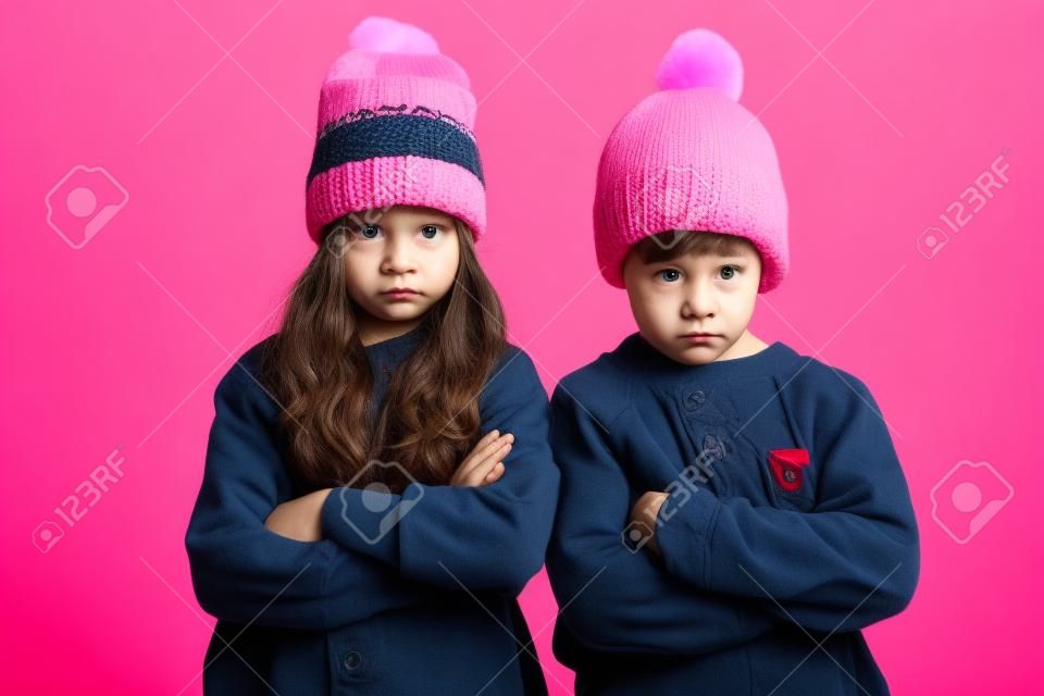 Foto de dos niños enojados disgustados aislados sobre fondo rosa con sombreros calientes. Mirando la cámara.