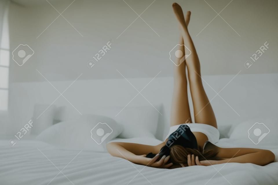 Portréja egy gyönyörű fiatal nő, ágyon, lábakkal fel a hálószobában ágyon