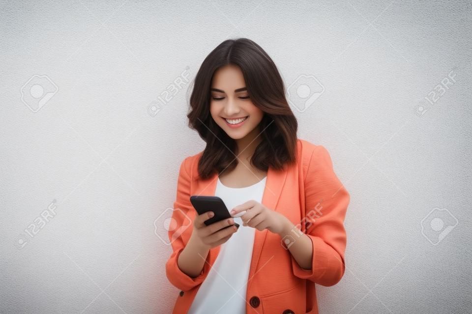 Image of young cute beautiful lady standing isolated over white wall background looking aside using mobile phone.