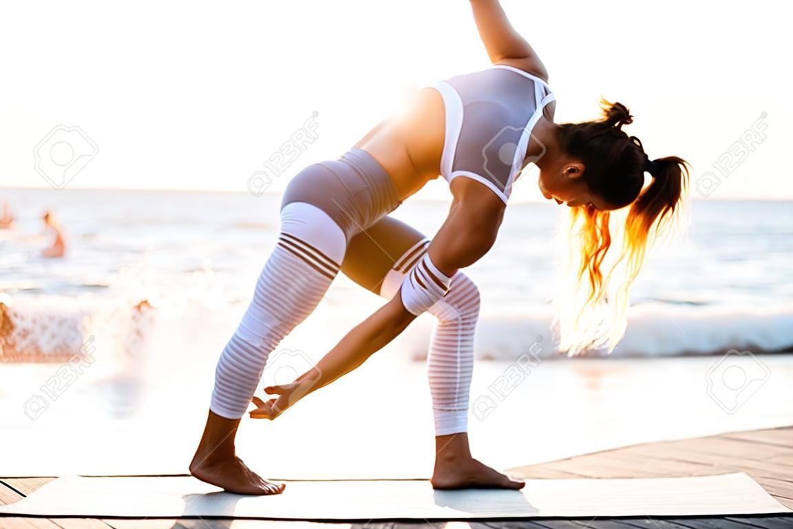 Beeld van verbazingwekkende sterke jonge fitness vrouw buiten in het strand maken yoga stretching oefeningen.