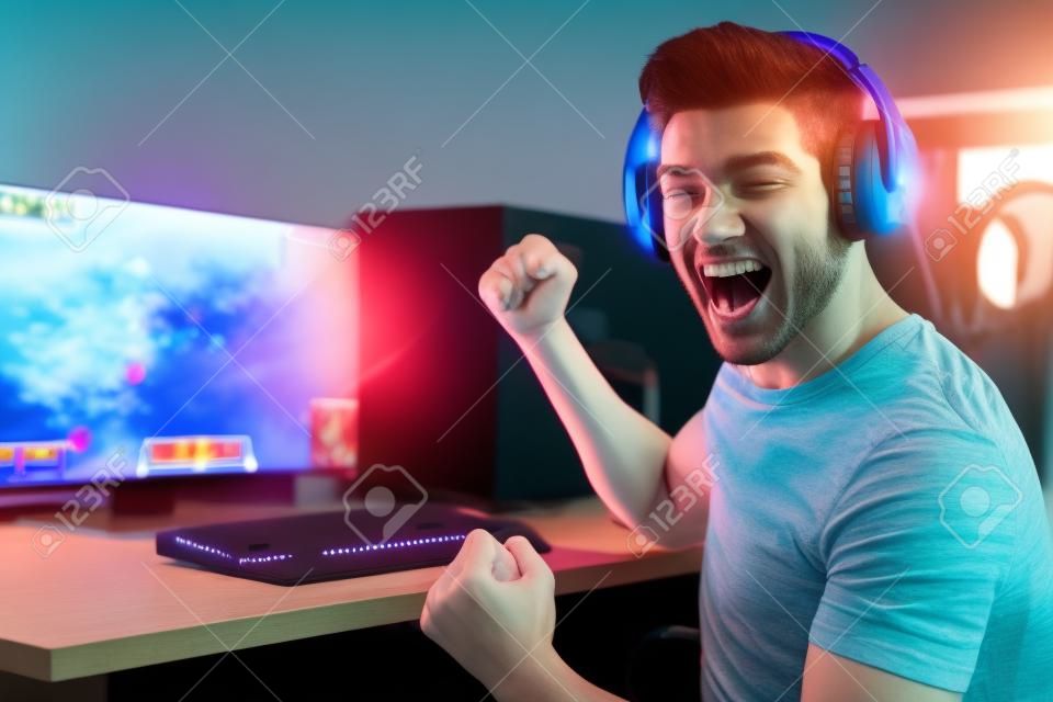 Porträt eines glücklichen Mannes, der Videospiele auf dem Computer spielt, Kopfhörer trägt und eine bunte Tastatur mit Hintergrundbeleuchtung verwendet