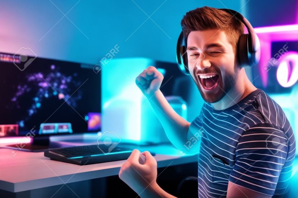 Porträt eines glücklichen Mannes, der Videospiele auf dem Computer spielt, Kopfhörer trägt und eine bunte Tastatur mit Hintergrundbeleuchtung verwendet