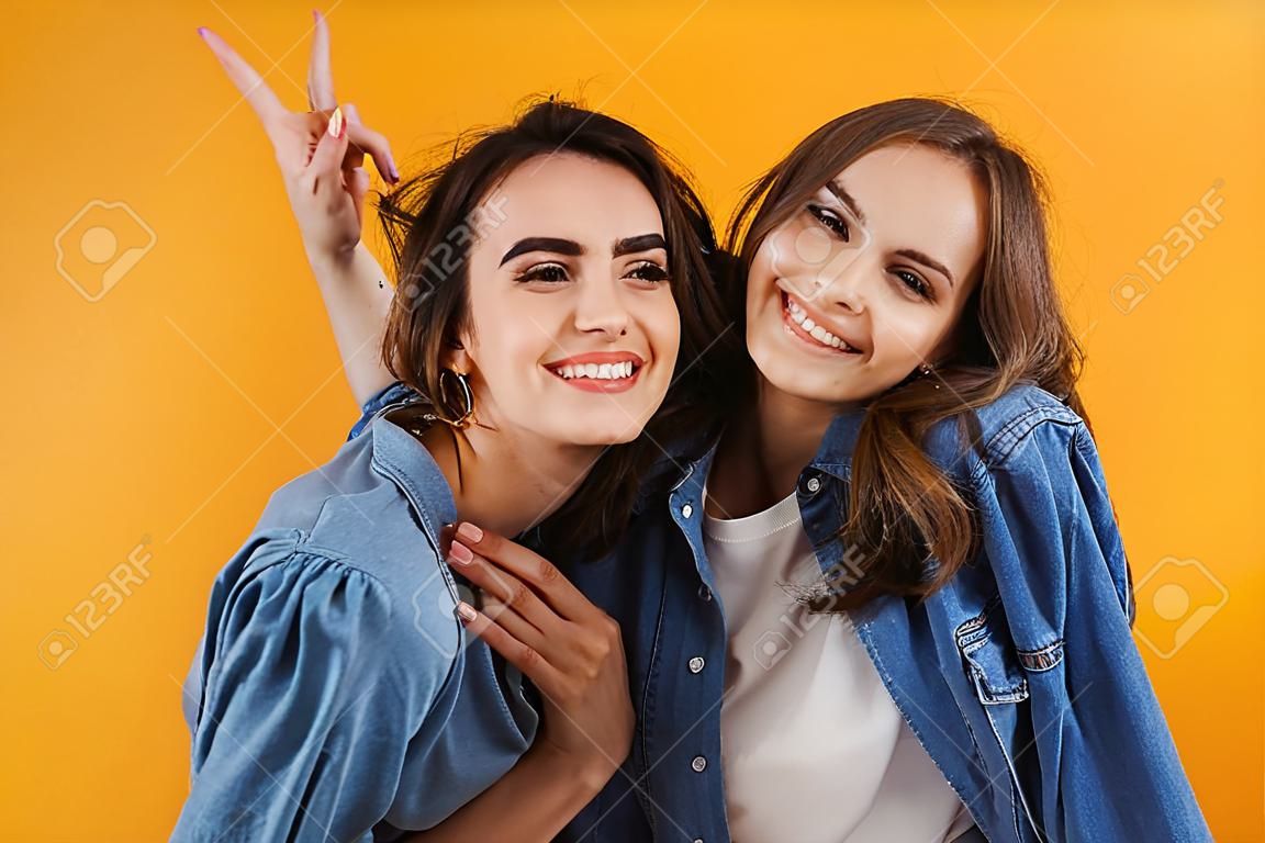 Imagem de feliz animado jovens mulheres amigos isolados sobre fundo de parede amarela tirar uma selfie pela câmera.