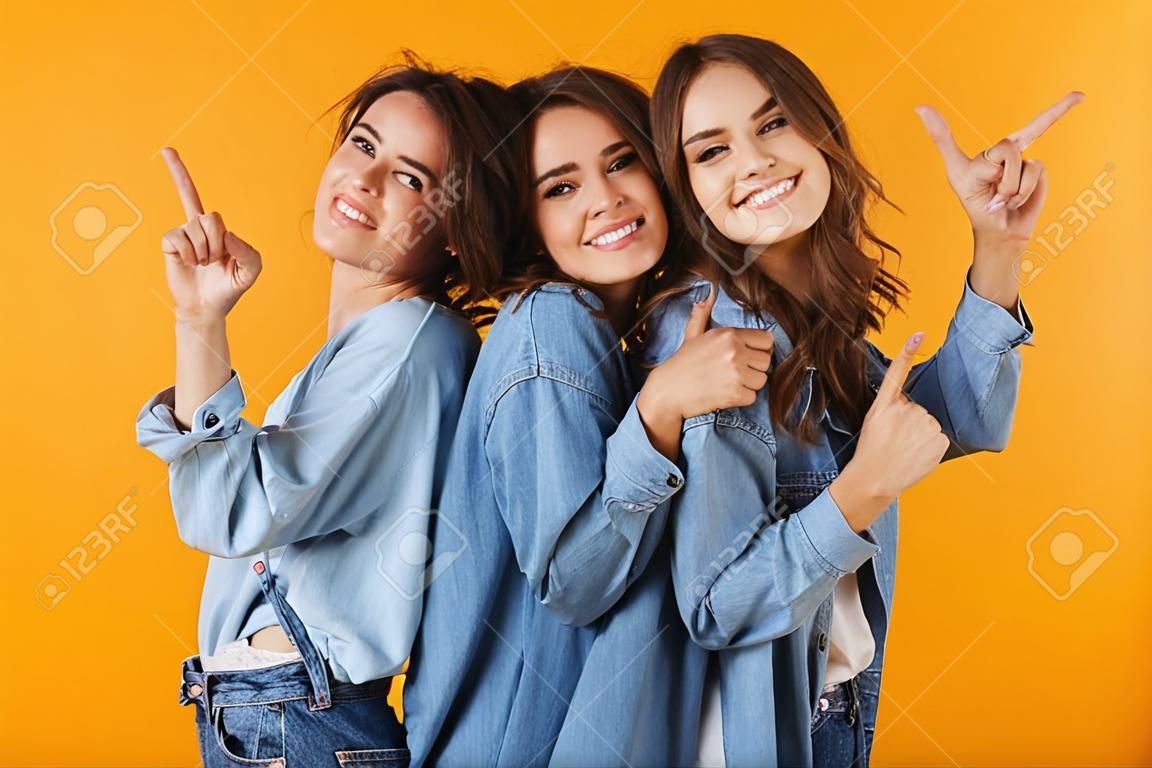 Photo of cute young women friends posing isolated over yellow background pointing.