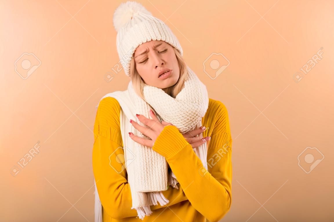 Photo of a displeased frozen woman wearing scarf and hat posing isolated over yellow wall background.