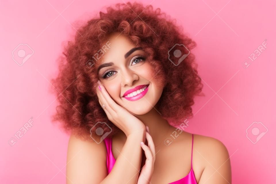 Portret close-up van prachtige krullende vrouw 20s dragen jurk glimlachend terwijl staan geïsoleerd over roze achtergrond