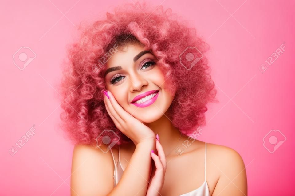Portret close-up van prachtige krullende vrouw 20s dragen jurk glimlachend terwijl staan geïsoleerd over roze achtergrond