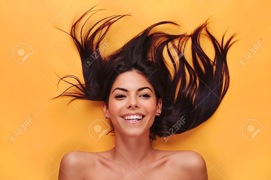Image of beautiful pleased happy young woman lies isolated on yellow background. Healthy hair concept.