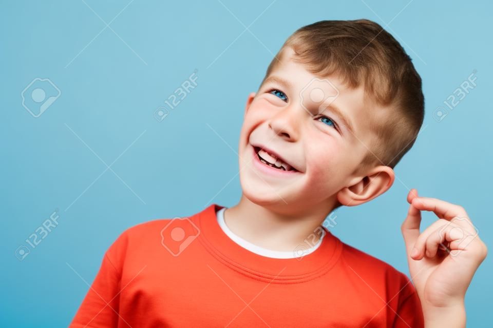 Image of happy caucasian boy 10-12y with freckles wearing white casual t-shirt and earpods looking at camera isolated over blue