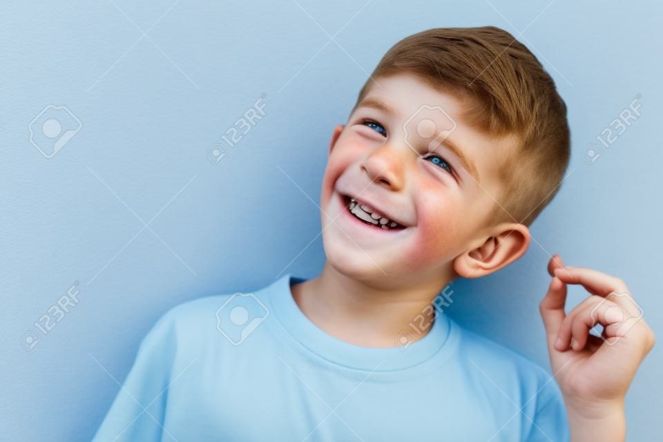 Image of happy caucasian boy 10-12y with freckles wearing white casual t-shirt and earpods looking at camera isolated over blue