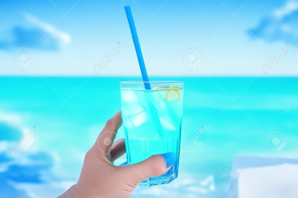背景にビーチと女性の手のビーチで青いさわやかなカクテル。