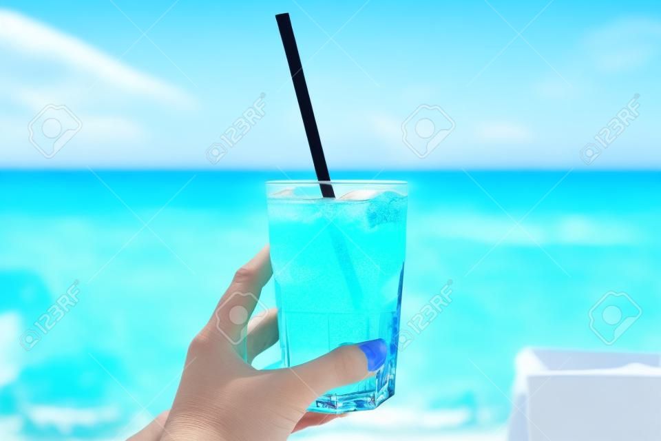 Blauer erfrischender cocktail am strand in der frauenhand mit strand im hintergrund.
