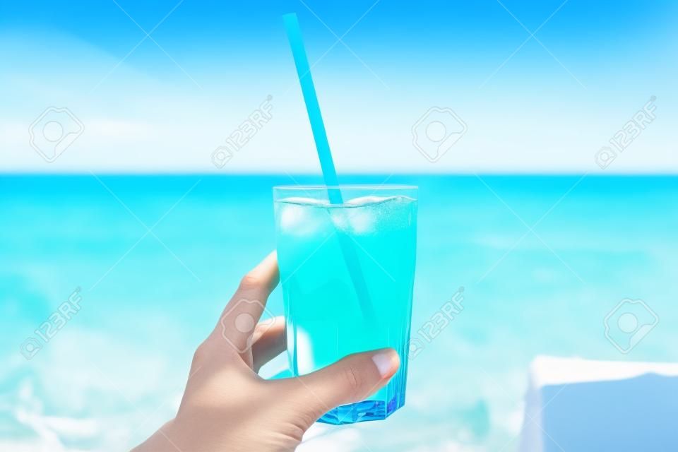 blue refreshing cocktail at the beach in the woman hand with beach on background .