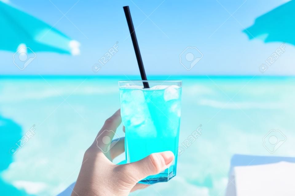 Blauer erfrischender cocktail am strand in der frauenhand mit strand im hintergrund.