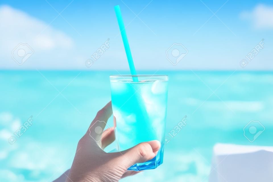 背景にビーチと女性の手のビーチで青いさわやかなカクテル。