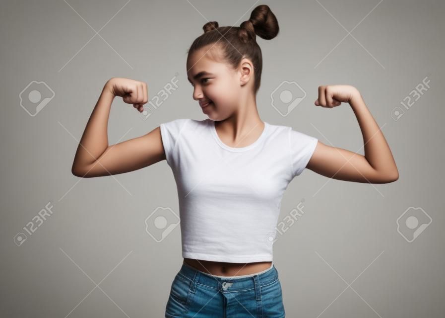 Retrato de menina adolescente engraçado levantou as mãos e mostra bíceps, isolado no fundo branco. Triste menina adolescente bonito mostra bíceps. Criança upset flexionando bíceps.