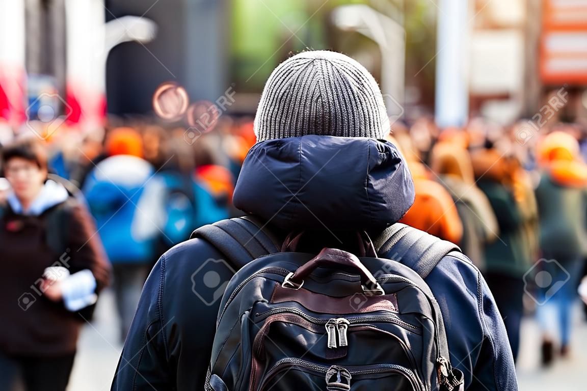 A man wearing a backpack is viewed from behind, as a large crowd of environmentalists is seen blurry in the background. with room for copy