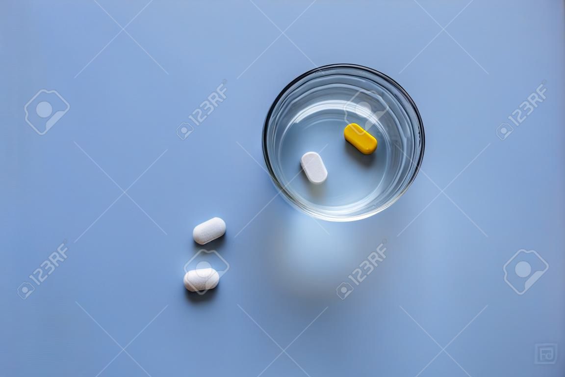 Un bicchiere d'acqua e una pillola su uno sfondo blu chiaro