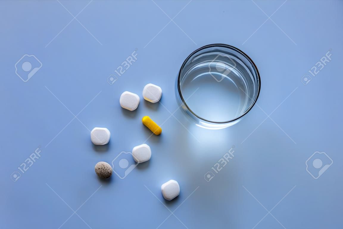 A glass of water and one pill on a blue plain background
