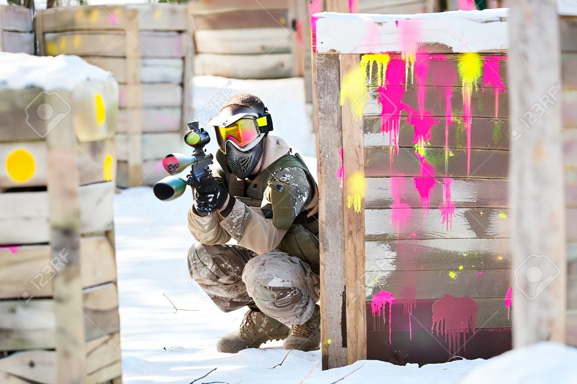 Paintball game in winter. Cool shooter behind fortification.