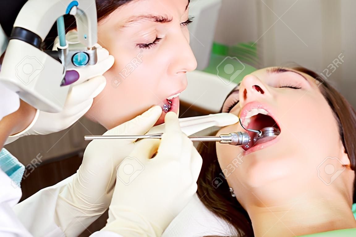 paciente jovem da mulher no dentista com boca aberta durante o procedimento de perfuração, tiro horizontal, close up