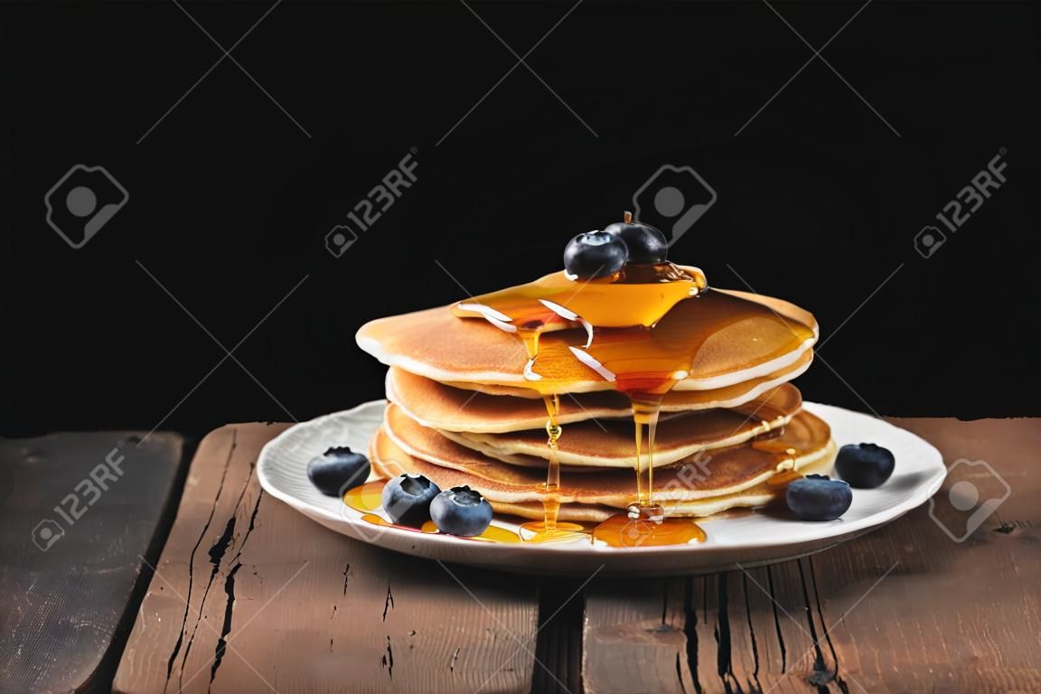 Naleśniki z jagodami i miodem na drewnianym stole w stylu rustykalnym. Deser na śniadanie na czarnym tle. Skopiuj miejsce na tekst.