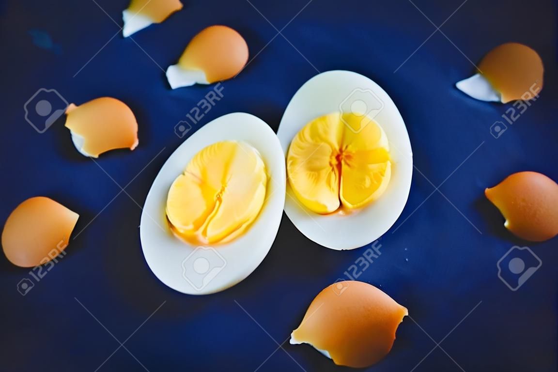 Su uno sfondo blu giacciono i resti di un guscio rotto e due metà di un uovo sodo con un tuorlo giallo brillante. Colazione. Cibo salutare.