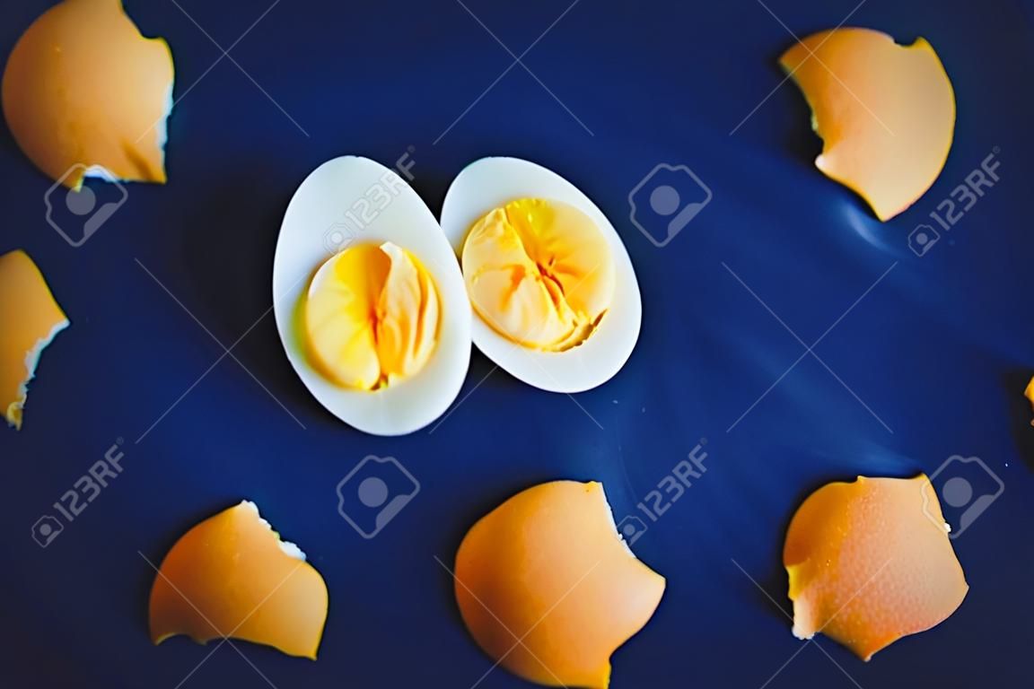 Su uno sfondo blu giacciono i resti di un guscio rotto e due metà di un uovo sodo con un tuorlo giallo brillante. Colazione. Cibo salutare.