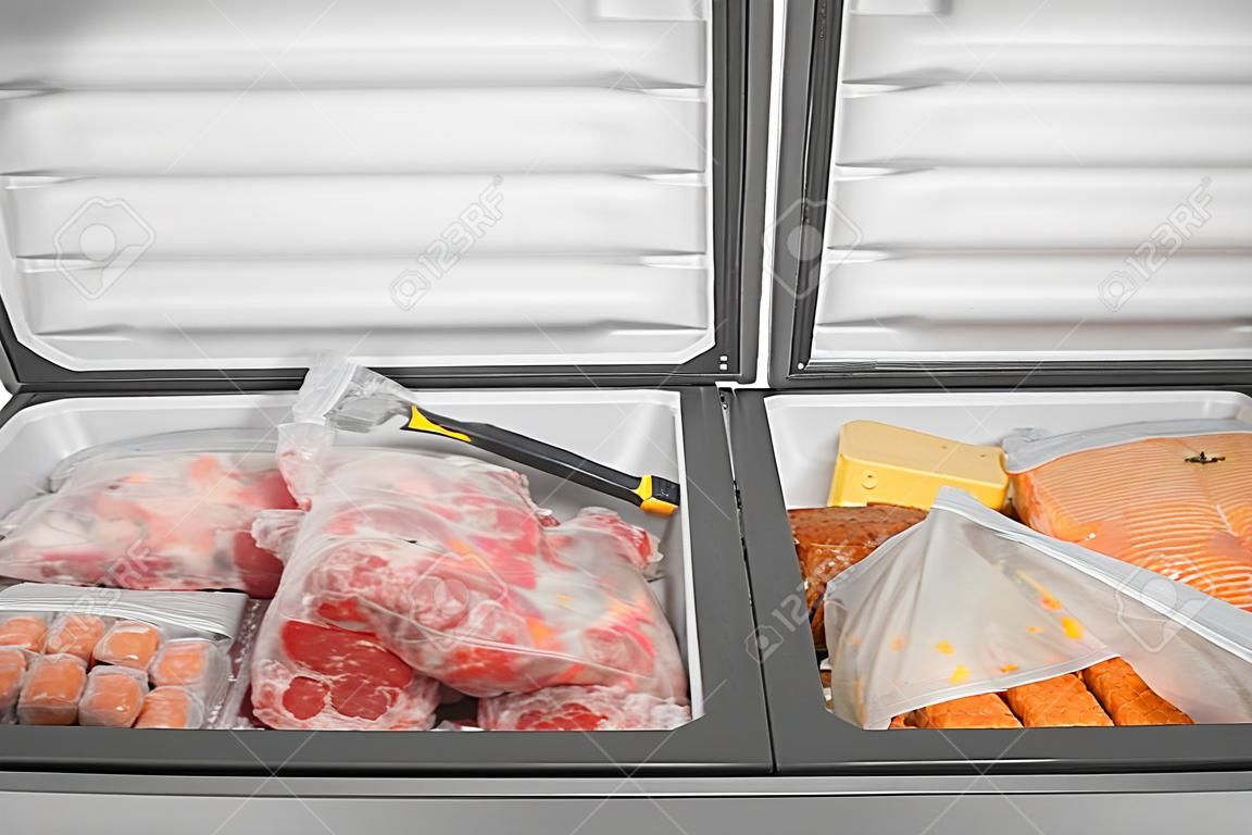 Tiefkühlkost im Gefrierschrank. Gefrorenes Fleisch und andere Lebensmittel in einem horizontalen Gefrierschrank bei geöffneten Türen einpacken. Lebensmittelkonservierung.