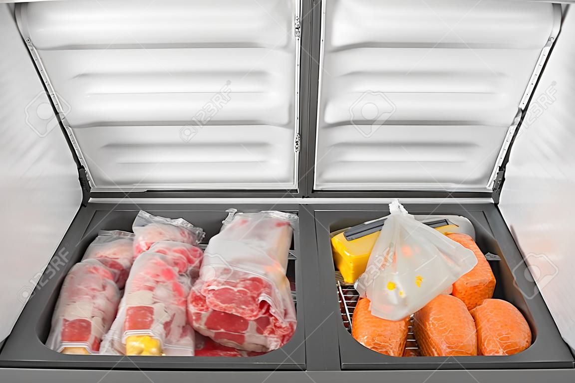 Alimenti congelati nel congelatore. Carne congelata insaccata e altri alimenti in un congelatore orizzontale con le due porte aperte. Conservazione del cibo.