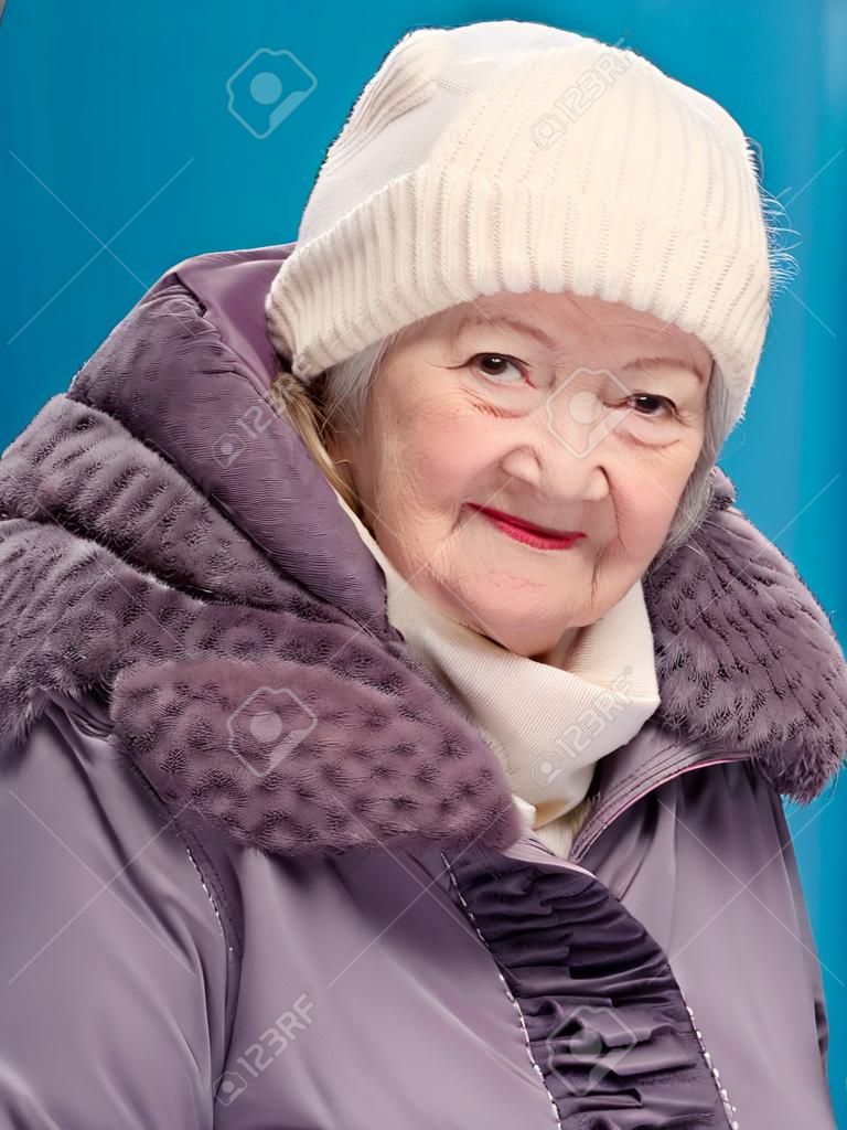 Portrait of smiling old woman in winterclothing on blue background