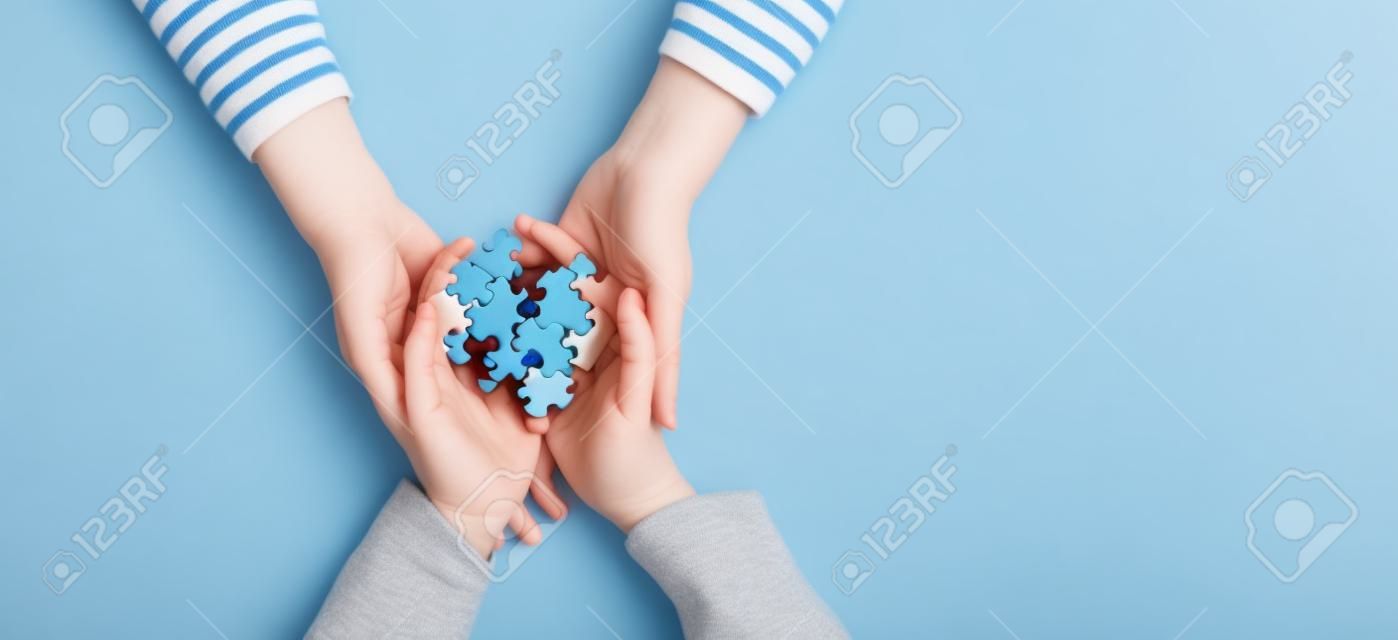 World autism awareness day concept. Woman and child hands holding puzzle heart on light blue background
