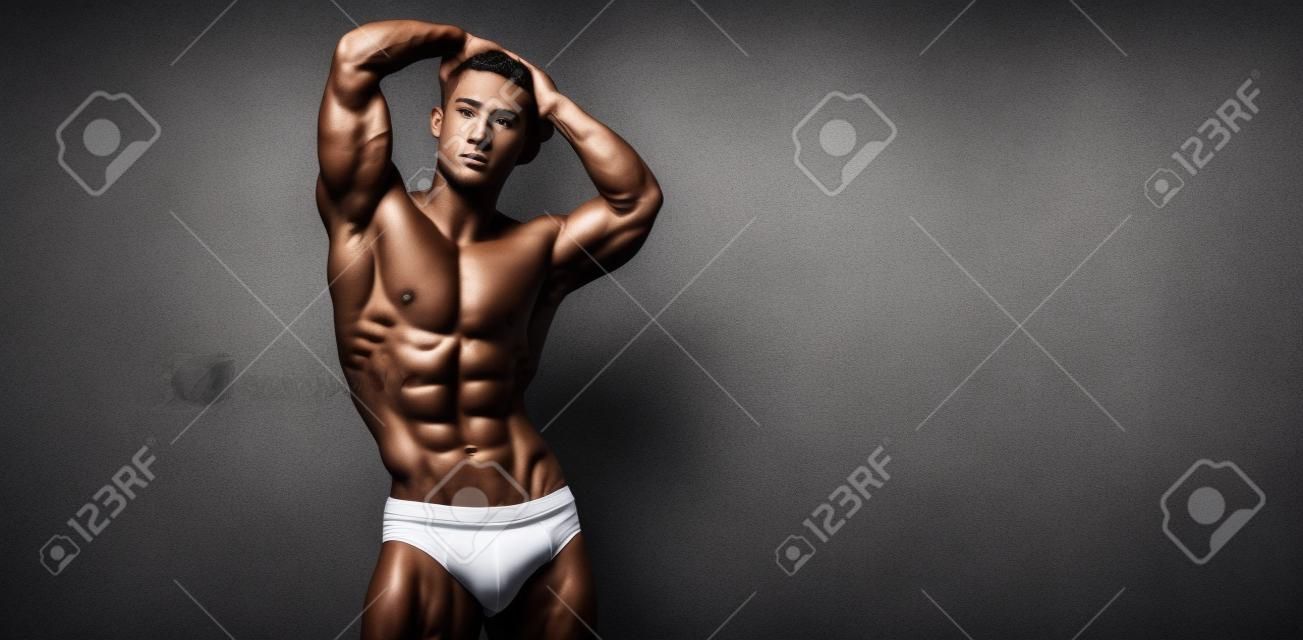 Young male athlete bodybuilder posing. Handsome athletic male power guy. Fitness muscular person. Young athlete showing muscles in the studio. six packs muscles posing shirtless on gray background.