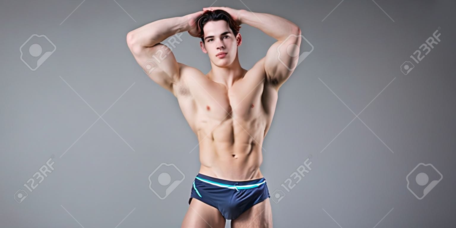 Young male athlete bodybuilder posing. Handsome athletic male power guy. Fitness muscular person. Young athlete showing muscles in the studio. six packs muscles posing shirtless on gray background.