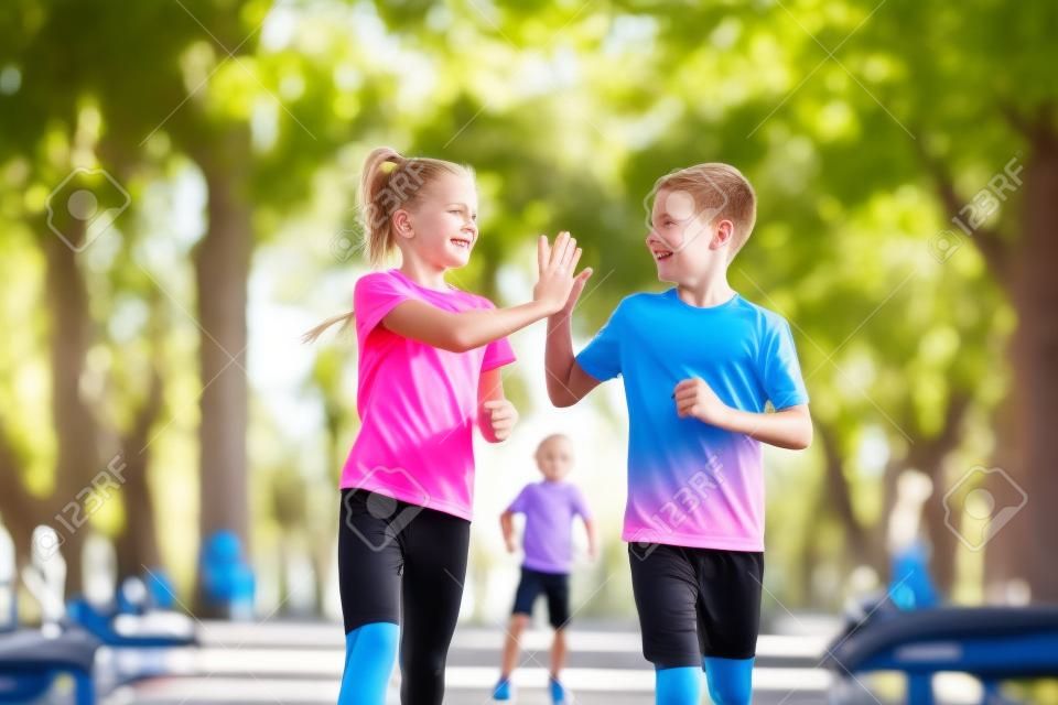 Sports and fitness in adolescence. Caucasian twins boy and girl run on the jogging track in the city park. Two children brother and sister for 10 years running on a rubberized outdoor treadmill.