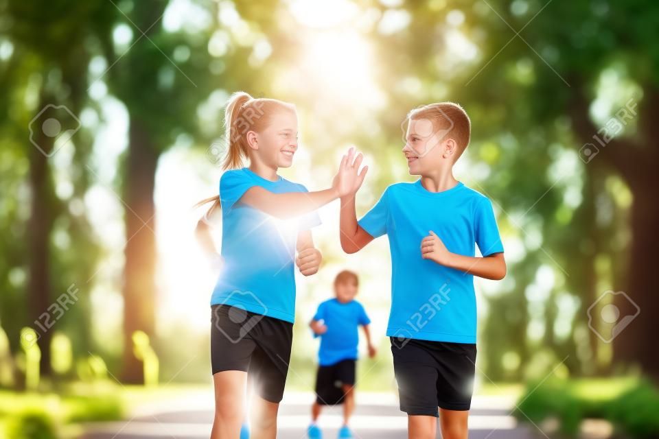 Sports and fitness in adolescence. Caucasian twins boy and girl run on the jogging track in the city park. Two children brother and sister for 10 years running on a rubberized outdoor treadmill.