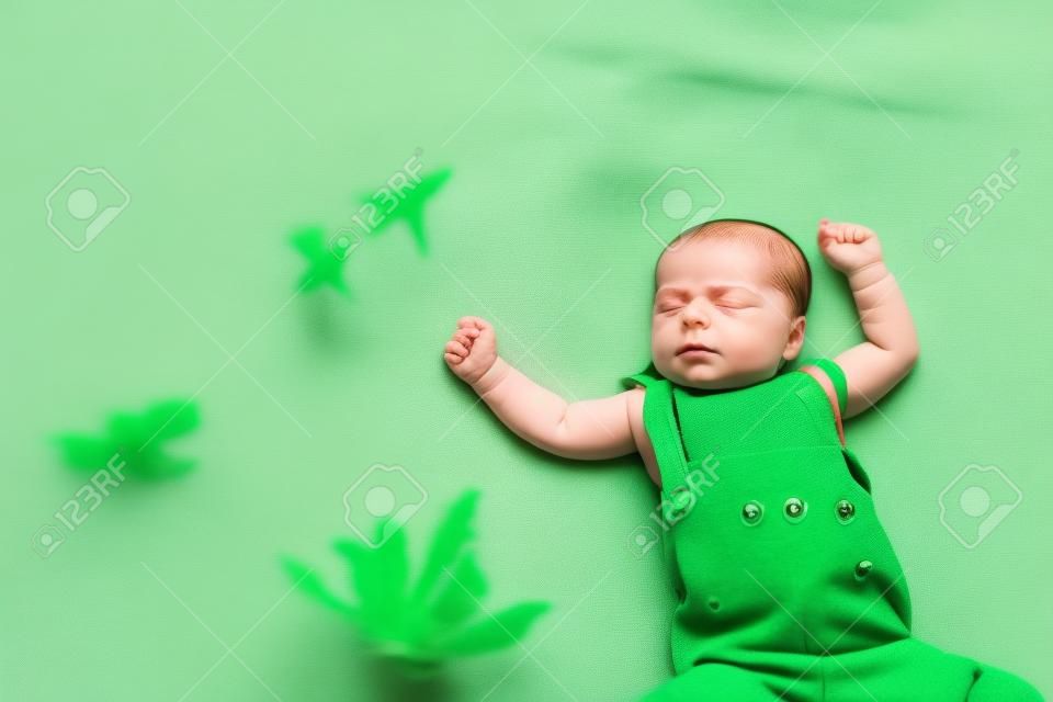 Little baby girl sleeps on a bed in a green suit, playmobile revolves over her.