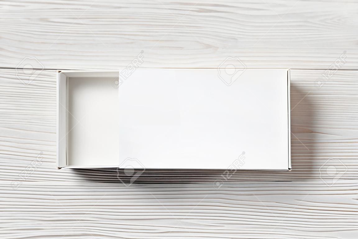 Blank white paper box on light wood table background. Package mockup. Branding mock up. Top view. Flat lay.