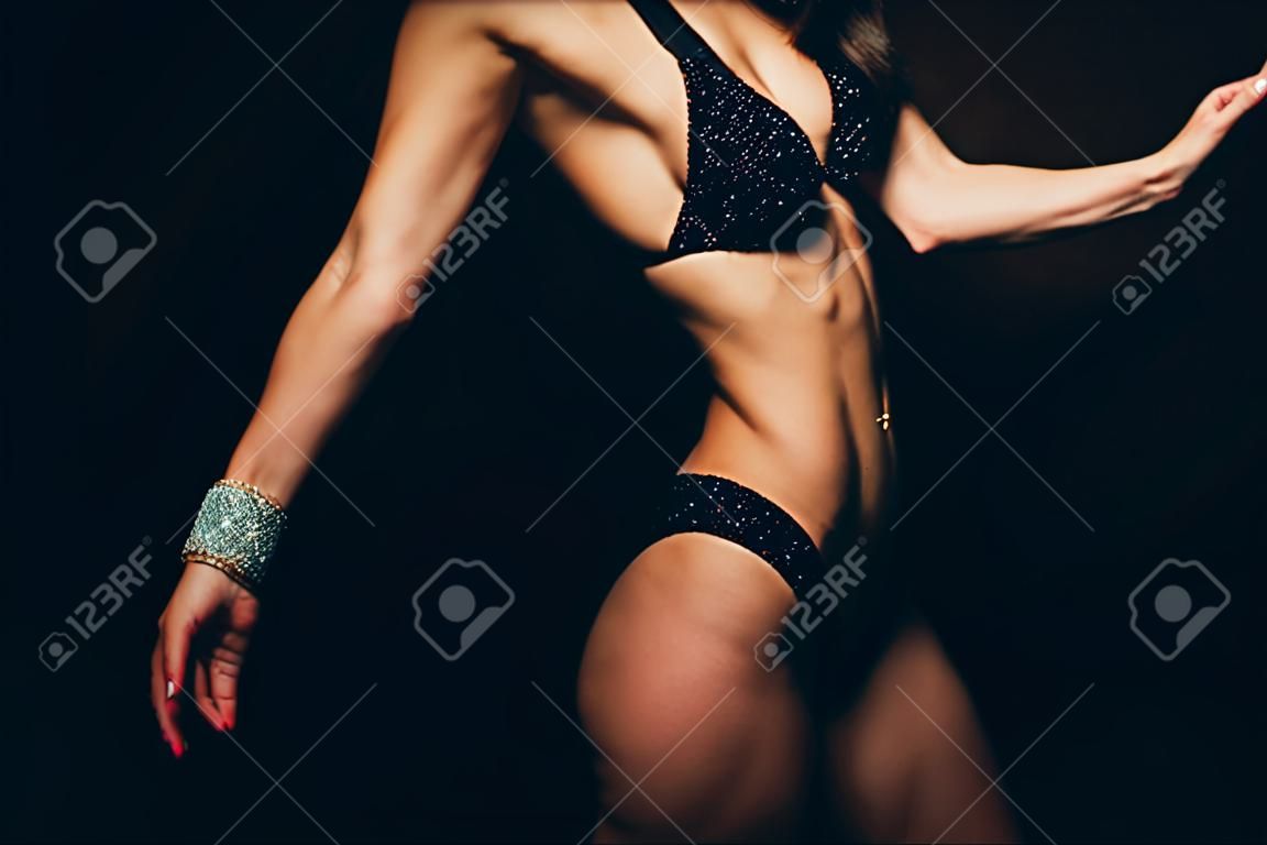 muskulöse, athletische junge Frau in einem farbigen Badeanzug auf schwarzem Hintergrund. Fitness. Muskulöser Körper. Torso. Bauchmuskeln