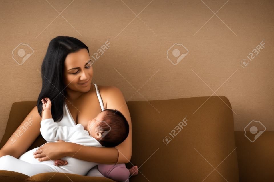 Eine Mutter, die ihren kleinen Jungen in ihren Armen stillt. braunes Sofa, Zuhause, weißes Top