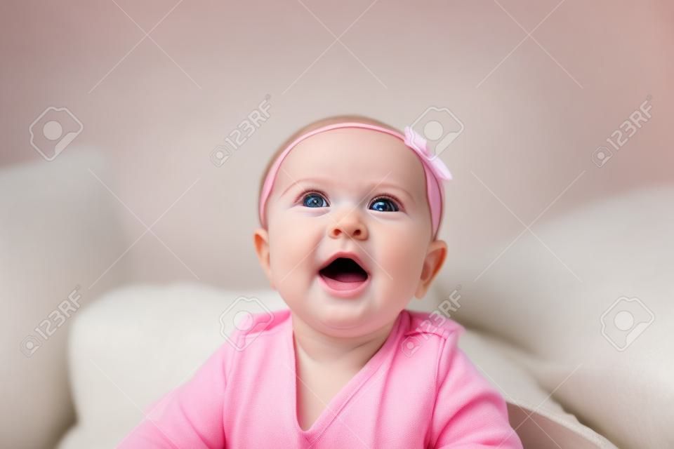 Dulce adorable niña acostada en un sofá mirando hacia la cámara. Bebé de 6-7 meses de edad en la parte superior del cuerpo de elevación del vientre.