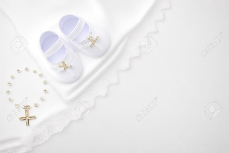 Christening background with baptism baby dress, shoes, and cross on pastel background