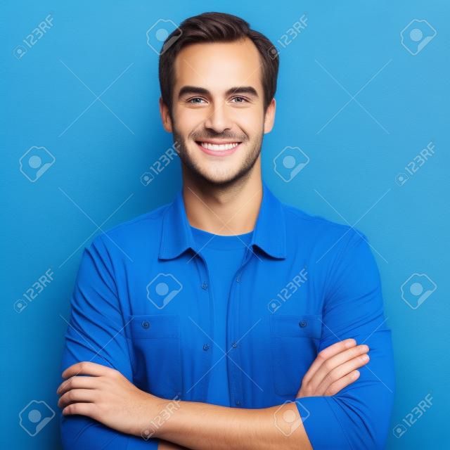 男の肖像画。笑顔の若い幸せな男。男性モデルは、腕を組んだポーズ。青の背景。カジュアルなファッション服、スタジオ写真の男。正方形の作曲画像。
